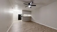 Located at 401 Small Hill Dr in Grand Prairie, TX, this single-story 2-bedroom, 1-bathroom home offers a practical and modern layout designed for comfortable everyday living. The open-concept living and kitchen area serves as the heart of the home, featuring durable wood-look plank flooring, neutral gray walls, a textured ceiling, and a ceiling fan with integrated lighting. The kitchen is equipped with white shaker-style cabinetry, black appliances including a refrigerator and gas range, a matte black gooseneck faucet, light countertops, and a peninsula that provides additional prep space and a natural divider from the living area. A pendant light fixture adds a decorative touch above the dining zone. Both bedrooms are carpeted, include ceiling fans, and receive natural light through window blinds. The primary bedroom offers a generous footprint. A dedicated walk-in closet with built-in shelving and wood-look flooring provides ample storage. The bathroom is a standout feature, showcasing a tub-shower combination with large-format marble-look tile surround, a built-in niche, and brushed nickel fixtures. A hallway connects the main living spaces, completing the efficient and well-organized floor plan.