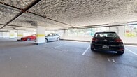 Located at 733 Goldstream Ave in Langford, BC, this expansive covered parking facility offers a substantial single-level layout designed to accommodate a large number of vehicles. The structure features a textured overhead ceiling with exposed piping and conduits running throughout, supported by evenly spaced white columns accented with yellow safety bands — a functional design choice that aids driver visibility and navigation throughout the facility. The floor is finished in durable asphalt with clearly painted white stall markings, including designated accessibility parking spaces equipped with standard wheelchair symbols and extra-wide berths. Perimeter fencing along the open sides of the structure allows natural light to filter in while maintaining security. Vehicle access is managed through automated roll-up garage doors at entry and exit points, with pedestrian access available via secured interior doors. A waste management area is incorporated within the facility. Emergency signage and fire suppression systems are visibly installed throughout, reflecting adherence to safety standards. The overall layout is open and easy to navigate, with wide drive aisles providing comfortable circulation. This well-maintained facility is well-suited to serve the needs of a nearby residential or commercial development.