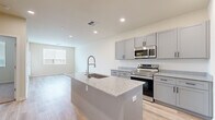This single-floor residence offers a clean, contemporary design with a thoughtful layout that balances open communal spaces and comfortable private areas. The kitchen serves as the heart of the home, showcasing gray shaker-style cabinetry, light granite countertops, a central island with an undermount sink and integrated seating, and a full suite of stainless steel appliances including a range, over-the-range microwave, and a large French door refrigerator. Light wood-look flooring runs throughout the kitchen and living areas, lending warmth and continuity to the open-concept floor plan. The living area is bright and airy, benefiting from natural light through slatted window blinds. The bedrooms feature plush wall-to-wall carpeting, ceiling fans, and well-sized windows that invite natural light. One bedroom connects to a generously sized walk-in closet outfitted with dual hanging rods and built-in shelving, providing ample storage. The bathroom is finished with a granite-topped vanity with an undermount sink, shaker-style cabinetry, a large mirror with overhead lighting, and a tiled tub-shower combination. Recessed lighting throughout and a neutral, warm color palette complete the polished, move-in-ready feel of this residence.