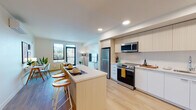 Unit B6 is a well-designed 1-bedroom, 1-bathroom residence that combines modern finishes with a functional, open layout. Light wood-toned flooring flows throughout the entire unit, creating a cohesive and airy feel.

The kitchen is thoughtfully appointed with flat-front cabinetry in a warm wood tone above and crisp white below, paired with a white tile backsplash and stainless steel appliances including a refrigerator, range, microwave, and dishwasher. A kitchen island with seating provides additional counter space and a casual dining option, while recessed lighting keeps the space bright and inviting.

The open-concept living area connects seamlessly to the kitchen, offering a comfortable and versatile layout. Large windows bring in natural light and frame views of the surrounding neighborhood and hills beyond.

The bedroom is a calm, private retreat featuring a sliding closet door and a tall, narrow window that frames scenic hillside and cityscape views. The clean white walls and warm flooring carry the unit's consistent modern aesthetic throughout.

The bathroom is clean and efficient, featuring a white vanity with an integrated sink, a mirrored medicine cabinet, and a combined tub and shower. Light wood flooring and crisp white walls complete the space with a minimalist finish.