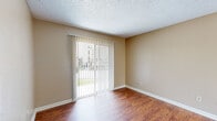 This single-floor residential unit offers a well-organized layout with a consistent, neutral color palette of warm beige tones throughout. The living area is bright and open, featuring rich hardwood-style flooring that extends through the main living spaces. A full-width sliding glass door fitted with vertical blinds fills the room with natural light and provides direct access to an outdoor area with greenery views, creating a welcoming and airy atmosphere. A ceiling fan with a light fixture serves the adjacent space, adding both functionality and comfort.

The galley-style kitchen is efficiently designed with warm wood cabinetry, light stone-look countertops, a double-basin stainless steel sink, and black appliances including a refrigerator, electric range, and dishwasher. Hardwood-style flooring continues seamlessly into this space.

The bedrooms are carpeted for added comfort and feature windows with blinds that bring in natural light. Each room offers closet access, and the textured ceilings are consistent throughout the unit.

The bathroom is well-appointed with a tiled tub-shower surround in a neutral stone finish, a wood-toned vanity with a light countertop, a large mirror, and hardwood-style flooring, completing the cohesive design of this practical and comfortable space.