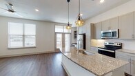 This well-appointed 1-bedroom, 1-bathroom residence offers a thoughtfully designed open-concept floor plan that seamlessly connects the kitchen, dining, and living areas. The kitchen serves as the centerpiece of the living space, showcasing a large island with granite countertops, an undermount sink, and geometric pendant lighting. Gray shaker-style cabinetry provides ample storage, while stainless steel appliances — including a refrigerator, range, and microwave — complete the modern aesthetic. Wood-look plank flooring flows throughout the main living areas, adding warmth and cohesion. The living area is bathed in natural light through multiple windows and offers direct access to a balcony through a glass door. The bedroom is a comfortable retreat featuring a ceiling fan, generous natural light from dual windows, and additional balcony access. The bathroom is elegantly finished with marble-style tile on the floors and walls, a soaking tub with a glass panel, and a granite-topped vanity with gray cabinetry. An additional room with a window provides flexible space for use as a home office or den. The unit's clean, neutral palette and contemporary finishes create a bright and inviting atmosphere throughout.