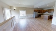 This well-appointed 2-bedroom, 2-bathroom single-story residence offers a generous and thoughtfully designed floor plan. The open-concept living and kitchen area creates a seamless flow, anchored by warm-toned luxury vinyl plank flooring that extends throughout the main living space. Classic white wainscoting panels line the lower walls, adding a refined architectural detail that lends both charm and character to the interior.

The kitchen is equipped with stainless steel appliances, including a French door refrigerator, microwave, and range, all complemented by rich medium-toned wood cabinetry and a light stone countertop. A kitchen island provides additional prep space and casual seating potential. Recessed lighting throughout ensures consistent, bright illumination, while a wall sconce adds a warm, decorative accent.

A well-placed window in the living area brings in natural light, enhancing the open and airy ambiance of the space. The vaulted ceiling detail in the living area adds vertical dimension and a sense of spaciousness. The neutral, warm beige wall tones pair harmoniously with the flooring and trim, creating a cohesive and inviting aesthetic throughout. This single-level home is ideal for those seeking comfortable, modern living with classic design touches.
