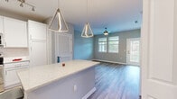 This well-designed single-floor residence offers a thoughtfully planned open-concept layout that seamlessly connects the kitchen, dining, and living areas. The kitchen is a standout feature, showcasing white shaker cabinetry, a classic subway tile backsplash, quartz countertops, and a full suite of stainless steel appliances. A central island with a light blue accent base provides additional prep space and serves as a natural gathering point. Geometric pendant lights add a modern, decorative touch overhead, while track lighting illuminates the workspace below. Light wood-look flooring flows throughout the main living areas, complemented by soft carpet in the bedrooms. The living area is bright and airy, benefiting from multiple windows that invite natural light and frame views of surrounding greenery, with a ceiling fan adding comfort. A glass-panel door opens to a private balcony. The bedrooms are generously sized, each offering natural light and ample closet space, including a walk-in closet off the primary bedroom. The bathroom features a white vanity with a quartz countertop, framed mirror, and wood-look tile flooring. An in-unit laundry area adds everyday convenience, completing this functional and modern home.