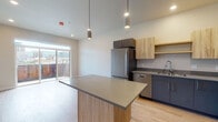 This contemporary 1-bedroom, 1-bathroom unit offers a well-designed, single-floor layout that blends modern aesthetics with practical functionality. The open-concept living and kitchen area serves as the heart of the unit, featuring light wood-tone flooring that extends throughout the space and contributes to a warm, cohesive feel.

The kitchen is thoughtfully appointed with a full suite of stainless steel appliances, including a refrigerator, range, microwave, and dishwasher. A two-tone cabinetry scheme pairs natural wood upper cabinets with sleek dark lower cabinets, complemented by a smooth grey countertop. A central kitchen island with matching finishes provides additional prep and dining space, while stylish pendant lighting hangs overhead to illuminate the area. A sliding glass door off the living area opens to a private balcony, inviting natural light and offering views of the surrounding cityscape.

The bedroom is a calm, well-proportioned retreat with neutral wall tones, continued wood-style flooring, and a bright window framing urban skyline views. The full bathroom features a tub-shower combination with tiled surround, a dark vanity with integrated sink, and wood-look flooring that ties back to the rest of the unit. Clean lines and a neutral palette define the overall aesthetic of this modern urban residence.