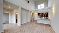 Located at 102 N Madison St in Waunakee, Wisconsin, this modern two-story residence is defined by its dramatic double-height ceilings on the main floor, creating an airy, open atmosphere filled with natural light from large upper-level windows. The main living area features light-toned hardwood-style flooring that flows seamlessly throughout, complementing the clean, neutral color palette of the walls and trim.

The open-concept kitchen is equipped with stainless steel appliances — including a refrigerator, electric range, and over-the-range microwave — set against rich dark cabinetry and light quartz countertops with a subtle tile backsplash. A peninsula counter provides additional workspace and a natural division between the kitchen and living area. A full bathroom on the main level includes a dark-toned vanity with a white countertop, a large mirror, and wood-look flooring.

An interior staircase leads to the upper level, where plush carpeting runs throughout the hallway and bedrooms. The bedrooms are generously proportioned, each featuring sliding-door closets with built-in shelving. An open railing overlook connects the upper level to the soaring main floor below. Wall sconces add warm accent lighting throughout, contributing to an overall ambiance that is clean, contemporary, and welcoming.