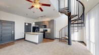 Located at 881 3rd Ave SW in Carmel, Indiana, this two-bedroom, three-bathroom two-story residence offers a well-designed layout spread across two floors. The main level showcases an open-concept living, dining, and kitchen area that feels bright and airy thanks to soaring ceilings and a ceiling fan overhead. The kitchen is outfitted with granite countertops, a large center island with an undermount sink, gray cabinetry, black appliances, a tile backsplash, and pendant lighting. Track lighting and wood-look flooring anchor the kitchen zone, which flows seamlessly into the carpeted living area. A dramatic wrought-iron spiral staircase serves as a striking architectural centerpiece, connecting the main floor to the upper level. Upstairs, the layout includes two carpeted bedrooms, each with ceiling fans and generous natural light from large windows. The primary bedroom offers a walk-in closet. Three full bathrooms are finished with tile flooring, soaker tubs with tiled surrounds, and gray vanities with white countertops. Additional conveniences include a dedicated laundry area with stacked washer and dryer, a pantry, and utility room. The upper floor also features a loft space, offering flexible use as an office or lounge.