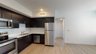 This single-floor residence offers a thoughtfully designed layout with a clean, contemporary aesthetic throughout. The kitchen serves as a standout feature, equipped with a full suite of stainless steel appliances including a refrigerator, range with microwave above, and dishwasher. Rich, dark espresso cabinetry extends from floor to ceiling, providing generous storage, while light-toned countertops and a stainless steel sink offer a striking contrast. Light wood-style flooring runs throughout the kitchen and adjoining open living area, lending warmth and continuity to the space.

The bedrooms are carpeted in neutral tones, creating a comfortable and quiet atmosphere. Each room benefits from window coverage with adjustable blinds, allowing control over natural light and privacy. One bedroom features a dual-window configuration that invites additional daylight and views of the surrounding exterior.

The bathroom is finished in a clean, minimalist style with light wood-look flooring, white surrounds, and a full soaking tub with shower combination fitted with brushed gold fixtures. A small window above the tub provides ventilation and soft natural light. Overall, the unit presents a cohesive, modern design with practical finishes suited for comfortable everyday living.
