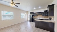 Located at 416 Majestic Crown Rd in Horizon City, TX, this single-story 2-bedroom, 1-bathroom home offers a well-designed layout with modern finishes throughout. The open-concept kitchen and living area serves as the heart of the home, featuring striking dark espresso cabinetry with raised-panel detailing, granite countertops, a tile mosaic backsplash, and black appliances including a full-size refrigerator and range. A peninsula provides additional counter space and casual seating. A pendant light and ceiling fan complement the living area, which receives natural light through blinds-fitted windows and a glass-panel exterior door that leads outside. Light wood-look laminate flooring runs throughout the entire home, creating a cohesive and easy-to-maintain aesthetic. The hallway connects the two bedrooms, bathroom, and closets. The primary bedroom is generously sized and includes access to a walk-in closet with dual hanging rods. The second bedroom also features a window with natural light. The full bathroom includes a tub/shower combo and clean white finishes. A dedicated laundry area with side-by-side washer and dryer hookups adds everyday convenience. Two closets provide ample storage throughout the home.