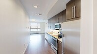 Located on the second floor at 80 Winooski Falls Way in Winooski, Vermont, Unit 204 is a thoughtfully laid-out residential unit that makes efficient use of its space. The interior is characterized by a clean, modern aesthetic with crisp white walls and consistent hard-surface flooring throughout the main living areas.

A welcoming hallway leads into the open-concept living and kitchen area, where natural light streams in through a large window, creating a bright and airy atmosphere. The galley-style kitchen is well-appointed with dark wood cabinetry, light countertops, and a full suite of stainless steel appliances, including a range, microwave, dishwasher, and refrigerator. A wall-mounted mini-split unit provides climate control in the living area.

The bedroom is a calm, carpeted retreat accessed via a sliding glass door, offering a quiet separation from the main living space. Recessed lighting and a baseboard heating system are present throughout.

The full bathroom features floor-to-ceiling stone-look tile surrounding a soaking tub and shower combination with a curved curtain rod, complemented by coordinating tile flooring for a cohesive, polished look.