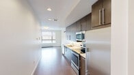 Located on the second floor at 80 Winooski Falls Way in Winooski, Vermont, Unit 204 is a thoughtfully laid-out residential unit that makes efficient use of its space. The interior is characterized by a clean, modern aesthetic with crisp white walls and consistent hard-surface flooring throughout the main living areas.

A welcoming hallway leads into the open-concept living and kitchen area, where natural light streams in through a large window, creating a bright and airy atmosphere. The galley-style kitchen is well-appointed with dark wood cabinetry, light countertops, and a full suite of stainless steel appliances, including a range, microwave, dishwasher, and refrigerator. A wall-mounted mini-split unit provides climate control in the living area.

The bedroom is a calm, carpeted retreat accessed via a sliding glass door, offering a quiet separation from the main living space. Recessed lighting and a baseboard heating system are present throughout.

The full bathroom features floor-to-ceiling stone-look tile surrounding a soaking tub and shower combination with a curved curtain rod, complemented by coordinating tile flooring for a cohesive, polished look.