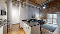Located in the heart of downtown St. Louis on Washington Avenue, this one-bedroom, one-bathroom loft unit blends industrial heritage with modern finishes. The open-plan living, dining, and kitchen area serves as the centerpiece of the home, anchored by dramatic soaring ceilings with exposed wood beams and visible ductwork that pay homage to the building's historic origins. Rich hardwood floors run throughout, complementing the striking exposed brick wall that spans the living area. Sliding glass doors open to a private balcony overlooking a bright interior atrium, flooding the space with natural light.

The kitchen is well-appointed with white cabinetry, dark granite countertops, black matte hardware, a double stainless steel sink, and a full suite of stainless appliances. A peninsula counter provides additional workspace and casual dining.

The bedroom features elevated ceilings, hardwood flooring, a mirrored sliding-door closet, and a calm, private atmosphere. The bathroom is clean and functional, offering a large sliding-glass enclosed shower, a wood-toned vanity, and stone-look tile flooring. Additional conveniences include in-unit laundry, a hallway, and two closets, making this a complete and practical urban retreat.