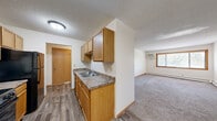 Located at 5641 69th Ave N in Brooklyn Park, Minnesota, this one-bedroom, one-bathroom unit offers a practical and efficiently designed single-floor layout. The kitchen is equipped with warm oak cabinetry, a double-basin sink, laminate countertops, and a black dishwasher, with hard surface flooring that transitions seamlessly into the combined dining and living area. The open-concept living space is carpeted and features a large window with wood trim that frames views of surrounding greenery, a wall-mounted air conditioning unit, and baseboard heating — providing year-round comfort. A textured ceiling runs throughout the unit, adding a classic residential character. The bedroom offers a well-proportioned, carpeted retreat with a window that allows natural light, a closet with sliding wood-panel doors, and baseboard heating. The bathroom is finished in neutral tones with wood-look tile flooring, a white vanity with a clean countertop, a wall-mounted medicine cabinet mirror, and a tiled tub/shower combination. A dedicated closet provides additional storage. The unit's straightforward layout and warm, neutral palette make it a functional and comfortable living space in a residential Brooklyn Park neighborhood.