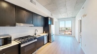 Located at 625 North 2nd Avenue in downtown Phoenix, AZ, this modern one-bedroom, one-bathroom unit offers a thoughtfully designed layout with contemporary finishes throughout. The open-concept kitchen and living area serves as the heart of the space, showcasing an exposed concrete ceiling that adds an industrial character. The kitchen is well-appointed with dark, flat-front cabinetry, a white tile backsplash, stainless steel appliances including a gas range, dishwasher, and refrigerator, complemented by matte black fixtures. Light wood flooring flows seamlessly through the main living area, enhancing the bright and airy atmosphere. A large window in the living area frames city views of the Phoenix skyline, flooding the space with natural light. The bedroom continues the clean aesthetic with white walls, light wood flooring, an exposed concrete ceiling, and a tall window offering additional city views. The bathroom features large-format floor tiles, a combination tub and shower with white tile surround and matte black fixtures, a floating wood vanity with a white countertop, and a backlit mirror. The unit is completed by an in-unit laundry area and a dedicated closet, providing practical storage solutions.