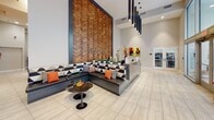 Located at 121 N Second St in Philadelphia's historic Old City neighborhood, this contemporary commercial space presents a well-designed, single-floor lobby that makes a strong first impression. The entrance features expansive floor-to-ceiling windows that flood the space with natural light and offer open views of the surrounding streetscape, creating a welcoming and transparent atmosphere.

At the heart of the lobby stands a sleek reception desk finished in dark gray with a granite-like surface, set against a dramatic full-height feature wall clad in layered wood panels arranged in a chevron pattern, bearing the "National" signage. Pendant lighting with elongated cylindrical fixtures adds a modern, architectural touch overhead.

A generously sized lounge area is anchored by a built-in L-shaped sectional sofa upholstered in a bold geometric black-and-white pattern, accented with orange and patterned throw pillows. Light-toned tile flooring extends throughout, lending a clean, professional feel. A high-top communal table with modern bar stools near the entrance provides an informal meeting or waiting area, complemented by a wall-mounted display screen.

Glass-paneled sliding doors lead to enclosed office spaces, maintaining visual connectivity while ensuring privacy. Above, a mezzanine level with metal railings overlooks the main floor, adding volume and a sense of dynamic vertical space to the overall design.
