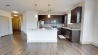 Located at 1201 Central Haven Dr in Mount Pleasant, South Carolina, this single-floor residence offers a thoughtfully designed open-concept layout that seamlessly connects the kitchen, dining, and living areas. The kitchen is a standout feature, showcasing rich dark espresso cabinetry extending to the ceiling, a subway tile backsplash, crisp white quartz countertops, and a full suite of stainless steel appliances including a refrigerator, range, microwave, and dishwasher. A generously sized white island with pendant lighting above serves as both a functional workspace and a casual dining area. Wood-style flooring runs throughout the main living spaces, adding warmth and continuity to the contemporary aesthetic. The open living area is bright and airy, benefiting from multiple windows that invite abundant natural light, complemented by a ceiling fan overhead. A sliding glass door provides additional access and light. The bathrooms are finished with dark vanity cabinetry, white quartz countertops, large framed mirrors, and wood-style flooring. The primary bathroom includes a walk-in closet with built-in shelving. A secondary bathroom features a clean, minimalist design. The overall ambiance is modern and cohesive, with neutral tones and quality finishes throughout.