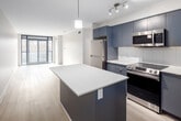 Located at 3385 Dundas Street West in Toronto, Unit 606 is a thoughtfully designed multi-bedroom suite offering four bedrooms, one full bathroom, and in-unit laundry within a efficiently organized single-floor layout. Light-toned laminate flooring runs throughout, lending a clean and cohesive aesthetic across all rooms.

The open-concept kitchen and living area serves as the heart of the unit. The kitchen features grey flat-panel cabinetry reaching the ceiling, quartz countertops, a white subway tile backsplash, stainless steel appliances including a refrigerator, electric range, and over-the-range microwave, and a central island with a contrasting blue base. The adjoining living area benefits from floor-to-ceiling windows and a sliding glass door that frames outdoor treetop views, filling the space with natural light.

The four bedrooms are finished with the same light flooring and neutral walls; several feature windows overlooking greenery. The primary bedroom offers direct access to the bathroom. The bathroom is finished in a contemporary style with grey vanity cabinetry, quartz countertops, a large mirror, and tile surround. A dedicated laundry closet houses a stacked Whirlpool washer and dryer unit. Two additional closets provide supplementary storage throughout the suite.