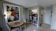 This single-floor space combines modern design with a warm, curated aesthetic. The open-concept layout seamlessly connects the living, dining, and kitchen areas, creating a cohesive and functional flow throughout.

The kitchen is neatly appointed with white cabinetry, under-cabinet lighting, and dark countertops. It opens directly to a breakfast bar fitted with elegant high-back bar stools in a soft silver-gray finish, making it an ideal spot for casual dining or entertaining.

Adjacent to the kitchen, a cozy dining nook features a round marble-topped table paired with a classic upholstered chair. A large, framed Museum of Modern Art print adds a bold artistic focal point to the space, infusing it with cultural character and visual interest.

The living area is finished with plush neutral carpeting and light gray walls that create a calm, sophisticated atmosphere. Subtle decorative accents — including metallic table accessories and sculptural wall pieces — add layers of personality without overwhelming the space.

The overall ambiance is refined yet approachable, blending contemporary furnishings with art-forward styling. The thoughtful use of color, texture, and décor throughout gives this space a distinctive, gallery-inspired residential feel.