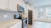 This single-floor unit presents a cohesive, modern aesthetic carried consistently across all living spaces. The kitchen is well-appointed with a full suite of stainless steel appliances, including a refrigerator, electric range, and over-the-range microwave. White shaker-style cabinetry extends to the ceiling, maximizing storage, while light quartz countertops and a classic subway tile backsplash complete the clean, contemporary look. Light hardwood-style flooring flows seamlessly from the kitchen into the adjoining living area, lending warmth and continuity throughout the unit. The living space is bright and open, benefiting from natural light through large windows fitted with horizontal blinds. A ceiling fan overhead adds both function and a finishing touch to the room. The bedroom is equally spacious and well-lit, featuring the same warm flooring, crisp white walls, and a ceiling fan. The bathroom maintains the unit's clean design language with a full soaking tub and shower combination, white tile surround, brushed gold hardware accents, white cabinetry, and matching hardwood-style flooring. Overall, the unit offers a bright, move-in-ready environment with thoughtful finishes and a consistent modern palette throughout.