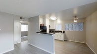 Located at 4300 Echo Ct in La Mesa, this single-story residence offers a thoughtfully designed open-concept layout that seamlessly connects the kitchen and living areas. The kitchen is a standout feature, showcasing white cabinetry, dark contrasting countertops, and a peninsula that doubles as a breakfast bar — ideal for casual dining or entertaining. A stainless steel sink sits beneath a window fitted with vertical blinds, allowing natural light to filter into the space. The kitchen is equipped with a refrigerator and additional appliances, with under-cabinet lighting adding a refined touch.

Light wood-style flooring runs throughout the main living areas, contributing to a clean, contemporary aesthetic. The neutral gray wall tones complement the white cabinetry and create a cohesive, modern palette. A textured ceiling adds character overhead, while flush-mount and pendant lighting fixtures provide ample illumination.

The adjoining living area is open and airy, with a sliding glass door or large window visible in the background, drawing in additional natural light. The overall ambiance is bright, functional, and well-maintained, making this La Mesa residence a comfortable and inviting single-floor home.