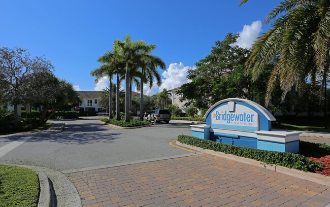 Inviting entrance to Bridgewater at Lake Osborne with palm trees and a sunny, welcoming atmosphere. - Bridgewater at Lake Osborne