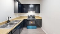 This 2-bedroom, 1-bathroom unit in Greeneville, TN offers a clean, modern aesthetic highlighted by light wood-look flooring throughout and a crisp white color palette. The open-concept living, dining, and kitchen area serves as the heart of the home, providing a flexible and functional layout. The kitchen is equipped with bold dark cabinetry, light wood-tone countertops, a stainless steel refrigerator, and a stainless electric range, creating a striking contrast against the bright surroundings. A long hallway, lined with dark-framed doors, connects the living area to the private quarters, lending a sense of depth and definition to the layout. Both bedrooms are well-proportioned and feature ceiling fans, light flooring, and natural light from windows with blinds. The primary bedroom offers a comfortable footprint with dedicated closet space, while both bedrooms benefit from additional storage across the unit's five closets. The full bathroom includes a clean white tub-shower combination with a rainfall-style showerhead and classic fixtures. A utility room and hallway round out the functional spaces. Textured ceilings add subtle character throughout, and the consistent use of dark door hardware and frames delivers a cohesive, contemporary feel.