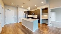 This well-appointed 960-square-foot apartment at 1774 Metro Avenue in Chula Vista, CA offers a modern single-floor layout with 2 bedrooms, 2 bathrooms, and 2 closets. The open-concept kitchen and living area serves as the heart of the home, featuring dark wood cabinetry, a large white quartz island with pendant lighting, stainless steel appliances including a French door refrigerator, gas range, and built-in microwave, all complemented by warm wood-look flooring. A built-in desk nook adds functional workspace. The living area extends naturally from the kitchen, with large windows that invite abundant natural light. The primary bedroom spans 160 square feet with plush carpeting, high ceilings, and direct access to a private en-suite bathroom. The primary bath features a dual-sink vanity with dark cabinetry, quartz countertops, a glass-enclosed walk-in shower, and wood-look flooring. The secondary bedroom also features soft carpeting and connects to a full bathroom complete with a shower-tub combo. Both bedrooms are served by dedicated closets with built-in shelving and hanging rods. Throughout the unit, neutral tones, recessed lighting, and clean architectural lines create a cohesive, contemporary ambiance.