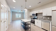 This well-designed one-bedroom, one-bathroom residence in Springfield, Missouri offers a thoughtfully organized single-floor layout that maximizes functionality and comfort. The open-concept kitchen and living area serves as the heart of the home, featuring crisp white shaker-style cabinetry, granite countertops, a stylish tile backsplash, and a full suite of stainless steel appliances including a gas range, microwave, dishwasher, and French door refrigerator. Pendant lighting and recessed ceiling fixtures illuminate the space, while light wood-style flooring flows seamlessly throughout, creating a cohesive and modern aesthetic. The living area is complemented by a ceiling fan and a window that brings in natural light. The bedroom is a comfortable, well-proportioned retreat with a window offering outdoor views and its own ceiling fan. A walk-in closet with wire shelving provides ample storage. The bathroom includes a walk-in shower, granite-topped vanity, and tile flooring. Additional practical spaces include a dedicated laundry room and a utility room. Neutral warm-gray wall tones and clean white trim throughout give the entire residence a fresh, move-in-ready feel.