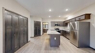 Located at 2003 9th St E in Menomonie, Wisconsin, this single-floor 2-bedroom, 1-bathroom residence offers a thoughtfully designed layout with modern finishes throughout. The open-concept kitchen is a standout feature, showcasing rich dark cabinetry, light granite-style countertops, stainless steel appliances including a refrigerator, range, microwave, and dishwasher, and a central island that provides additional prep and seating space. Recessed lighting and light wood-look flooring enhance the bright, contemporary feel of the kitchen and living area. The living space is anchored by a fireplace and includes a ceiling fan overhead, creating a comfortable and inviting atmosphere. Two bedrooms feature plush carpeting, ceiling fans, and large windows that frame peaceful wooded views, filling each room with natural light. The primary bedroom offers generous proportions and direct access to a closet and the shared bathroom. The bathroom is finished with a dark wood vanity with a stone-top sink, a full tub-shower combination, and matching light flooring. Dark-trimmed doors and consistent neutral tones tie the design together, giving the entire space a cohesive, modern aesthetic.