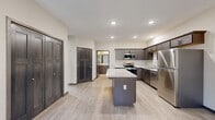 Located at 2003 9th St E in Menomonie, Wisconsin, this single-floor 2-bedroom, 1-bathroom residence offers a thoughtfully designed layout with modern finishes throughout. The open-concept kitchen is a standout feature, showcasing rich dark cabinetry, light granite-style countertops, stainless steel appliances including a refrigerator, range, microwave, and dishwasher, and a central island that provides additional prep and seating space. Recessed lighting and light wood-look flooring enhance the bright, contemporary feel of the kitchen and living area. The living space is anchored by a fireplace and includes a ceiling fan overhead, creating a comfortable and inviting atmosphere. Two bedrooms feature plush carpeting, ceiling fans, and large windows that frame peaceful wooded views, filling each room with natural light. The primary bedroom offers generous proportions and direct access to a closet and the shared bathroom. The bathroom is finished with a dark wood vanity with a stone-top sink, a full tub-shower combination, and matching light flooring. Dark-trimmed doors and consistent neutral tones tie the design together, giving the entire space a cohesive, modern aesthetic.