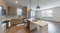 This single-floor residence at 3613 SW Durham Dr in Durham, NC offers a thoughtfully designed open-concept layout with contemporary finishes throughout. The kitchen serves as the centerpiece of the living area, showcasing wood-toned cabinetry, a farmhouse-style sink, stainless steel appliances including a refrigerator with ice maker, range, and built-in microwave. A spacious island with a white quartz countertop provides additional prep space and seating, illuminated by a pair of stylish pendant lights. Wood-look flooring extends through the main living areas, complementing the neutral color palette and recessed lighting overhead. Multiple windows allow natural light to fill the open living space, creating a bright and welcoming atmosphere.

The bedrooms feature plush carpeting, ceiling fans, and windows that bring in natural light. Each room offers generous proportions and direct access to well-equipped bathrooms. One bathroom includes a walk-in glass-enclosed shower with white subway tile, a single-sink vanity with wood cabinetry, and wood-look tile flooring. A second bathroom features a tub-shower combination with matching subway tile. A walk-in closet with built-in wire shelving provides practical storage. The overall design balances modern aesthetics with functional, comfortable living.