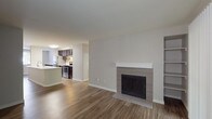 This single-floor residence offers a well-organized layout with a variety of functional living spaces. The open-concept living and dining area is anchored by a tiled fireplace with a white mantel, built-in shelving, and hardwood-style flooring that extends throughout the main areas. Vertical blinds cover a sliding glass door, allowing natural light to fill the room. The living area flows seamlessly toward the kitchen, which features dark espresso cabinetry, stainless steel appliances including a refrigerator and range, and a generous white quartz countertop peninsula with an undermount sink — ideal for both meal preparation and casual dining.

The bedrooms are carpeted for comfort, with one featuring a distinctive bay window configuration that brings in notable natural light and outdoor views of surrounding greenery, along with a private exterior door. A baseboard heating system is present in multiple rooms. The primary bedroom includes a connected bathroom, while a second full bathroom is also available, both outfitted with dark wood vanities, quartz countertops, and a tub-shower combination. Additional storage is accessible via closets visible throughout the layout.