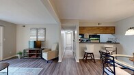 This single-floor, 2-bedroom, 2-bathroom residence in Indianapolis, IN offers a thoughtfully designed layout that maximizes functionality and comfort. The living room is bright and inviting, anchored by hardwood-style flooring and large sliding glass doors that open to a private patio, filling the space with natural light and offering pleasant outdoor views of lush greenery. Adjacent to the living area, the dining room features a stylish pendant chandelier and direct sightlines to the kitchen, creating a seamless flow for everyday living and entertaining. The galley-style kitchen is well-equipped with warm wood cabinetry, dark countertops, black appliances, and a double basin sink, complemented by a breakfast bar that connects to the dining area. A central hallway leads to both bedrooms, each carpeted for comfort. The primary bedroom is generously sized with a large closet and a window overlooking the outdoors. Six total closets throughout the home provide ample storage. Both bathrooms are finished with wood-tone vanities and dark countertops, with one featuring a tub-shower combination. The entrance and hallway connect all rooms efficiently, completing this practical and comfortable single-level home.