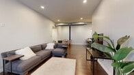 This well-appointed 2-bedroom, 2-bathroom unit in Birmingham, AL offers a thoughtfully designed single-level layout with modern industrial-chic character. The open-concept living, dining, and kitchen area forms the heart of the home, anchored by rich dark hardwood flooring throughout and recessed lighting overhead. Exposed silver ductwork adds an urban loft aesthetic to the bright, airy living room, which features tall ceilings and large windows dressed in sheer curtains that fill the space with natural light.

The kitchen is a standout, showcasing charcoal gray cabinetry with gold hardware, a white quartz waterfall island with bar seating, marble-look tile backsplash, globe pendant lighting, and stainless steel appliances. A dedicated dining area flows seamlessly from the kitchen.

Both bedrooms are comfortably sized with access to natural light and ample closet space. The unit's bold teal interior doors with gold hardware serve as a striking design element throughout the hallway connecting the rooms.

The two bathrooms are elegantly finished with large-format gray tile, herringbone tile flooring details, glass-enclosed walk-in showers with black framing, and modern oval mirrors with globe sconce lighting. Additional conveniences include in-unit laundry, making this a complete and refined urban residence.