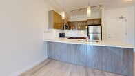 Located at 2578 James St in Abbotsford, BC, this well-appointed one-bedroom, one-bathroom unit offers a thoughtfully designed open-concept layout with modern finishes throughout. The kitchen is a standout feature, showcasing warm wood-tone cabinetry, a peninsula with a light quartz countertop, stainless steel appliances including a fridge, stove, built-in microwave, and dishwasher, and stylish pendant lighting. Light wood-look flooring flows through the main living area, complementing the bright, airy ambiance created by a large sliding glass door that invites natural light and provides outdoor views. The living area is open and functional, offering a comfortable everyday living space. The bedroom features soft carpet flooring, a generous built-in closet with double doors, and sun-filled windows that create a calm retreat. The bathroom is finished with clean white tile, a full soaker tub with overhead shower, and a modern vanity. A dedicated in-suite laundry area with a stacked washer and dryer adds practical convenience. The unit's clean, contemporary palette of whites and natural wood tones creates a cohesive and welcoming atmosphere throughout.