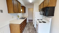 This 2-bedroom, 1-bathroom single-floor residence offers a functional and straightforward layout with classic design elements throughout. The galley-style kitchen is a standout feature, showcasing rich, warm-toned wood cabinetry on both upper and lower levels, light countertops, and a full suite of white appliances including an electric coil range and refrigerator, complemented by an overhead microwave. Wood-look flooring runs the length of the kitchen, adding a clean, durable finish. The living area is generously proportioned, featuring plush carpeting, a baseboard heating system, and large windows that invite abundant natural light. A wall-mounted air conditioning unit and sliding door provide additional comfort and access. Both bedrooms are carpeted and well-lit, each equipped with a ceiling fan and windows offering natural views of surrounding greenery. Baseboard heaters are present in each bedroom for year-round comfort. The bathroom maintains a clean, classic aesthetic with a white vanity, mirrored medicine cabinet, chrome fixtures, and a fully tiled shower surround. The overall ambiance of this residence is practical and comfortable, with timeless design details that provide a welcoming, livable environment.
