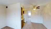 This single-floor Boulder residence presents a straightforward, functional layout designed for everyday living. The main living area features neutral wall-to-wall carpeting that adds warmth underfoot, while white walls and a textured ceiling keep the space feeling bright and clean. A ceiling fan with a light fixture is centrally positioned, providing both air circulation and ambient lighting to the room.

Adjacent to the living area, the compact kitchen is outfitted with dark wood cabinetry, a white refrigerator, and a light-colored countertop. The kitchen's tile flooring distinguishes it from the carpeted living space, creating a natural separation between the two areas. A partial wall divides the kitchen from the main room, adding subtle definition without fully closing off the space.

A louvered closet door along one wall provides convenient built-in storage. A doorway visible from the main living area leads to an additional room with a window that allows natural light to filter through, enhancing the overall brightness of the interior. The layout flows efficiently from room to room, making the space practical and easy to navigate. The overall ambiance is clean, understated, and move-in ready.