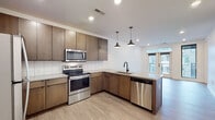 Located at 500 W Broad St in Columbus, Ohio, this single-floor residence showcases a thoughtfully designed, contemporary interior with a cohesive modern aesthetic throughout. The kitchen is a standout feature, equipped with rich warm-toned wood cabinetry, a white subway tile backsplash, stainless steel appliances including a range, microwave, dishwasher, and refrigerator, and light countertops that complement the overall palette. Pendant lighting adds a stylish accent above the kitchen workspace, while recessed lighting ensures a bright, functional environment. Light wood-style flooring flows seamlessly through the kitchen and into the open living area, which is filled with natural light from large floor-to-ceiling windows and glass-paned French doors that open to an outdoor space, offering views of the surrounding urban neighborhood. The living area provides a clean, versatile canvas with crisp white walls and recessed lighting overhead. The bathroom is finished with large-format tile flooring, a glass-enclosed walk-in shower adorned with white tile, and a vanity with warm wood cabinetry. An adjacent walk-in closet with wire shelving offers generous storage. The unit's clean lines, neutral tones, and modern finishes create a polished and functional living environment in the heart of Columbus.
