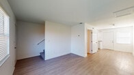 This two-floor residence offers a straightforward, functional layout designed for comfortable everyday living. The main level features an open living area finished with light-toned hardwood-style flooring that extends throughout, creating a cohesive and airy feel. A staircase with carpeted treads connects the two floors, while panel-style doors and clean white walls maintain a consistent, bright aesthetic throughout the space.

The kitchen is well-appointed with white shaker-style cabinetry, granite-look countertops, black appliances including a refrigerator and electric range with overhead ventilation, and a stainless steel sink. An adjacent pantry with built-in shelving provides convenient additional storage. A half bathroom on the main level features hardwood-style flooring, a wall-mounted light fixture, and a small window for ventilation.

The upper level hosts the bedrooms, each fitted with plush carpeting and windows dressed with horizontal blinds that admit natural light. One bedroom features light hardwood-style flooring and a generous window. Spacious closets with double panel doors and built-in hanging rods offer substantial storage. The full bathroom upstairs includes a tub-shower combination, a toilet, and a white vanity, all finished with warm hardwood-style flooring.