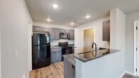 This thoughtfully designed single-story, one-bedroom, one-bathroom unit offers a cohesive layout across six distinct areas, including an entrance, kitchen, hallway, closet, bathroom, and bedroom. Light wood-look laminate flooring runs throughout the space, tying each room together with a warm, consistent aesthetic.

The kitchen serves as a functional centerpiece, featuring rich gray-toned cabinetry, granite-look countertops, and a full suite of black appliances including a refrigerator, range, and over-the-range microwave. A peninsula with an undermount sink and matching countertop provides additional prep space and a casual dining area.

The living area is bright and open, with neutral gray walls, hardwood-style flooring, and a ceiling fan with integrated lighting. Sliding glass doors lead to a private balcony, allowing abundant natural light to fill the room and offering an outdoor retreat.

The bedroom is a comfortable, well-proportioned space with a ceiling fan, a window with blinds for natural light and privacy, and access to a dedicated closet.

The bathroom features a distinctive blue-painted vanity with granite-look countertops, an undermount sink, modern matte black fixtures, and a well-lit mirror—adding a touch of personality to an otherwise neutral palette.