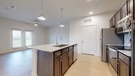 This single-story, one-bedroom, one-bathroom unit is thoughtfully designed to maximize functionality within a comfortable footprint. The open-concept kitchen and living area serves as the heart of the space, anchored by a central island with a granite countertop, undermount sink, and dark espresso cabinetry accented by brushed nickel hardware. Pendant lights hang above the island, complementing recessed ceiling lighting throughout. Stainless steel appliances, including a refrigerator, range, microwave, and dishwasher, are paired with a light subway tile backsplash, lending the kitchen a clean, contemporary aesthetic. Light hardwood-style flooring flows seamlessly through every room, enhancing the sense of openness. A ceiling fan is present in both the living area and the bedroom. The bedroom offers a comfortable, well-proportioned layout with a large window framing outdoor greenery and a dedicated closet for storage. The full bathroom features a dark-cabinet vanity with a granite countertop, a large mirror, and a glass-enclosed shower. An in-unit laundry area accommodates a full-size top-loading washer, adding everyday convenience. Neutral white walls throughout create a bright, move-in-ready environment.