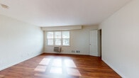 Located at 62 Settler Rd in Plymouth, Massachusetts, this single-floor residence offers a thoughtfully laid-out living space with a clean, neutral aesthetic throughout. The main living area is bathed in natural light streaming through large windows, highlighting the rich, warm-toned hardwood flooring that extends across the primary living spaces. The open feel of the living area is complemented by crisp white walls and a wall-mounted HVAC unit for year-round comfort.

The kitchen is efficiently designed in a galley-style layout, featuring warm wood cabinetry, granite-patterned countertops, tile flooring, and black appliances including a dishwasher and range. A window above the counter provides natural light and a view of the surrounding neighborhood.

The bedrooms offer a comfortable, quiet retreat, each finished with plush wall-to-wall carpeting and white walls. One bedroom includes a closet and direct access to the hallway, while additional closet space is available throughout. A wall-unit air conditioner and windows with views to the exterior are present in one of the bedrooms.

The full bathroom is finished with white tile flooring, a single-sink vanity with white cabinetry, and a tub-shower combination framed by white tile surround, offering a clean and functional space. Overall, the unit presents a bright, well-maintained interior in a residential Plymouth setting.