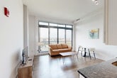 Located at 1151 4th St SW in Washington, DC, this one-bedroom unit offers a well-organized, single-floor layout designed for efficient urban living. The open-concept living and dining area is the heart of the home, featuring warm hardwood-style flooring, crisp white walls, and expansive floor-to-ceiling windows that flood the space with natural light and frame sweeping views of the Washington skyline. A private balcony is accessible directly from the living area, extending the living space outdoors. The kitchen integrates seamlessly into the main living area and includes stainless steel appliances, including a full-size refrigerator with ice maker, and sleek white cabinetry. The bedroom is a calm, neutral retreat with light carpet flooring, a high transom window for additional natural light, and direct access to a dedicated walk-in closet with built-in shelving and hanging storage. A hallway connects the main spaces and leads to the in-unit laundry room, which is equipped with a stacked Bosch washer and dryer — a practical and convenient amenity. Throughout the unit, the clean, minimalist aesthetic and thoughtful layout make the most of every square foot, creating a comfortable and functional living environment in the heart of the nation's capital.