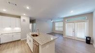 Located at 3880 FM 2920 in Spring, Texas, this 1-bedroom, 1-bathroom residence offers a thoughtfully designed single-level layout with modern finishes throughout. The open-concept kitchen and living area serves as the heart of the home, anchored by a central island with granite countertops, an undermount sink, and stainless steel appliances including a French door refrigerator, range, and microwave. Crisp white shaker cabinetry and a subway tile backsplash complete the kitchen's clean, contemporary aesthetic. Light wood-look flooring flows through the kitchen and living area, where a ceiling fan, multiple windows with blinds, and a glass-panel entry door with transom window allow for generous natural light. The bedroom is carpeted for comfort, features dual windows, and is equipped with its own ceiling fan, creating a bright and relaxing retreat. An adjacent walk-in closet offers built-in shelving and hanging rods for ample storage. The full bathroom includes a tub-shower combination with tile surround, granite-topped vanity with white cabinetry, and wood-look flooring, maintaining a cohesive design throughout. Neutral wall tones and recessed lighting contribute to a clean, inviting ambiance across the entire space.