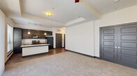 Located at 881 3rd Ave SW in Carmel, Indiana, this one-bedroom, one-bathroom residence offers a thoughtfully designed open-concept layout that seamlessly connects the living, dining, and kitchen areas. The kitchen is a standout feature, showcasing rich dark cabinetry that reaches toward the ceiling, a granite-topped island with a built-in wine rack and undermount sink, stainless appliances, a tile backsplash, and pendant lighting complemented by a track lighting system. Wood-look tile flooring runs throughout the kitchen and dining areas, while plush carpet adds warmth to the living room and bedroom. Large windows allow natural light to fill the main living space and bedroom, the latter of which also includes a ceiling fan. The bathroom is finished with tile flooring, a dual-sink dark vanity with framed mirrors, and a tiled soaking tub and shower combination. Three closets provide generous storage throughout the unit, including a spacious walk-in closet accessible from the bathroom. A dedicated laundry area houses a full-size front-loading washer and dryer. The consistent use of dark trim, paneled doors, and neutral tones throughout gives the space a cohesive, contemporary character.