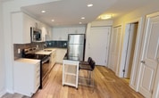 Located at 950 24th Street in the heart of Washington, DC's desirable Georgetown neighborhood, this single-floor residence offers a thoughtfully designed layout with modern finishes throughout. The open-concept kitchen is a standout feature, showcasing crisp white cabinetry extending to the ceiling, a slate-toned subway tile backsplash, light hardwood flooring, and a full suite of stainless steel appliances including a refrigerator, electric range, and over-the-range microwave. Bright recessed lighting illuminates the space, while a compact island with bar seating adds functional versatility for dining or entertaining. The kitchen flows seamlessly into the main living area, which shares the same warm hardwood flooring and is bathed in natural light. The bedroom is finished with soft, neutral-toned carpeting and features a window with horizontal blinds that frames views of the surrounding neighborhood's greenery. The bathroom presents a clean, contemporary aesthetic with a wide vanity offering ample drawer storage, a white countertop with an undermount sink, and a large mirror. The overall ambiance of the residence is modern and understated, with neutral wall tones and consistent, quality finishes creating a cohesive and comfortable living environment.