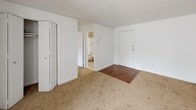 This single-floor, one-bedroom, one-bathroom unit provides a functional and straightforward layout suited for comfortable everyday living. The living area features neutral wall-to-wall carpeting, white paneled walls, and baseboard heating, creating a clean and manageable space. A window allows natural light to filter in, brightening the room. The entryway transitions between hardwood-style flooring and carpet, offering a clear delineation between spaces. A closet within the living area provides convenient storage access.

The kitchen is equipped with rich, dark wood cabinetry offering ample upper and lower storage, a granite-style countertop, a stainless steel sink, and a white gas range. Wood-look flooring runs throughout the kitchen, and a wall-mounted light fixture adds warm illumination to the space.

The bedroom is generously proportioned with soft carpeting underfoot, white walls, and a built-in closet. It maintains the same clean, minimal aesthetic found throughout the unit.

The bathroom features a full soaking tub with a tub/shower combination, accented by chrome fixtures and classic tile detailing along the upper surround, providing a clean and functional bathing space. Overall, the unit presents a no-frills, practical living environment with consistent finishes throughout.