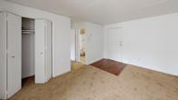 This single-floor, one-bedroom, one-bathroom unit provides a functional and straightforward layout suited for comfortable everyday living. The living area features neutral wall-to-wall carpeting, white paneled walls, and baseboard heating, creating a clean and manageable space. A window allows natural light to filter in, brightening the room. The entryway transitions between hardwood-style flooring and carpet, offering a clear delineation between spaces. A closet within the living area provides convenient storage access.

The kitchen is equipped with rich, dark wood cabinetry offering ample upper and lower storage, a granite-style countertop, a stainless steel sink, and a white gas range. Wood-look flooring runs throughout the kitchen, and a wall-mounted light fixture adds warm illumination to the space.

The bedroom is generously proportioned with soft carpeting underfoot, white walls, and a built-in closet. It maintains the same clean, minimal aesthetic found throughout the unit.

The bathroom features a full soaking tub with a tub/shower combination, accented by chrome fixtures and classic tile detailing along the upper surround, providing a clean and functional bathing space. Overall, the unit presents a no-frills, practical living environment with consistent finishes throughout.