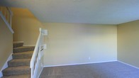 This two-story residence offers a straightforward and functional layout spread across two levels, connected by a staircase featuring classic white balusters and a sturdy handrail. The interior is finished with neutral, warm-toned walls that create a calm and inviting atmosphere throughout. Soft carpeting covers the floors, adding comfort underfoot and contributing to a cozy residential feel. The ceilings carry a textured finish, a common and durable architectural detail that adds subtle visual depth to the space. Clean white baseboards provide a crisp contrast against the warm wall tones, lending a tidy and well-maintained appearance. The open wall space offers significant flexibility for furniture arrangement and personalization. Overall, the space presents a clean, move-in-ready environment with a simple, classic aesthetic that suits a variety of living styles.