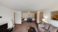 This single-floor residence offers a thoughtfully arranged layout that balances comfort and functionality across its interconnected living spaces. The living room serves as the heart of the home, featuring plush carpeting, a sliding glass door with vertical blinds that opens to an outdoor view, and an additional side window that fills the space with natural light. A wall-mounted air conditioning unit and baseboard heating ensure year-round comfort.

The dining area flows naturally from the living room and features carpeted flooring, a ceiling light fixture, and a large closet with warm wood-toned sliding doors — a practical storage solution just steps from the main living space. A breakfast bar with bar-stool seating connects the dining area to the kitchen, offering a casual eating option.

The galley-style kitchen is efficiently designed with ample white cabinetry trimmed in warm wood tones, a double stainless steel sink, and durable hardwood-style flooring. White appliances, including a refrigerator, range, and dishwasher, are neatly integrated throughout.

The bedroom is a calm retreat with carpeted floors, a window with blinds for natural light, and a textured ceiling. A second flexible room provides additional space, featuring a window and wall-mounted shelving. The full bathroom includes a shower/tub combination, vanity with storage, and hardwood-style flooring.